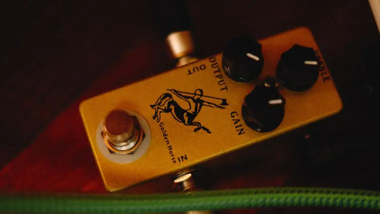 Pedal de efectos dorado para guitarra sobre fondo oscuro